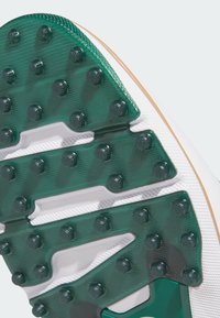 Suola esterna in gomma verde e trasparente con tacchetti circolari, suola intermedia bianca e accenti marroni, con motivi testurizzati per la trazione.
