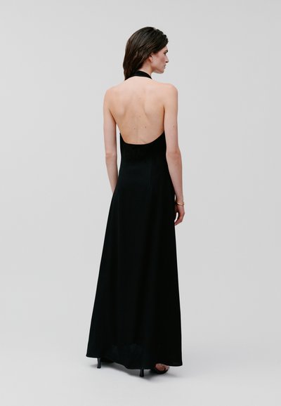 Black halter-neck maxi dress with an open back; smooth fabric, fitted bodice, and flowing skirt. Minimalist design, ankle-length.