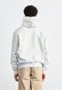 Sudadera con capucha gris de corte relajado y puños acanalados, combinada con pantalones beige. La tela parece suave y tiene una textura lisa.