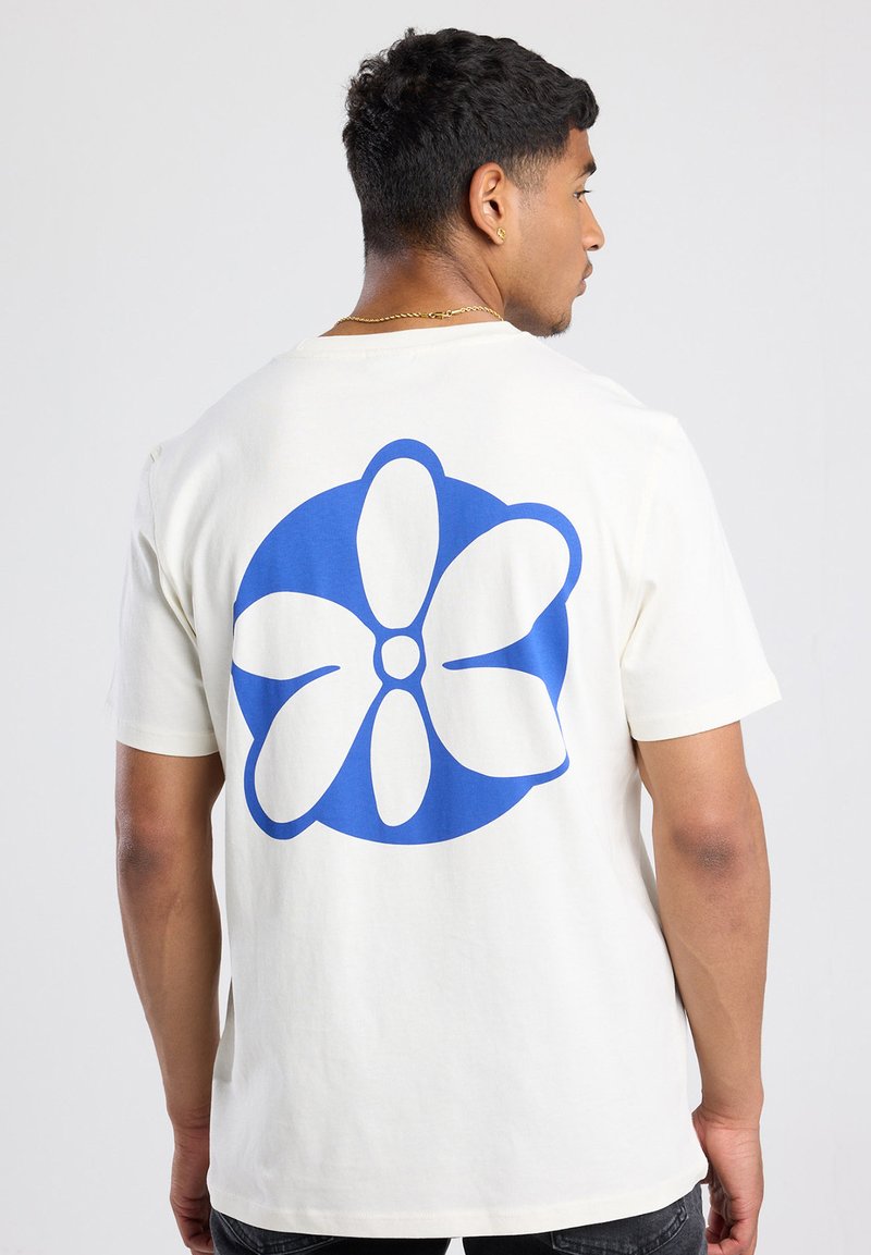 Crème-kleurige katoenen t-shirt met een grote blauwe bloemenafdruk op de achterkant. Korte mouwen en een relaxte pasvorm.