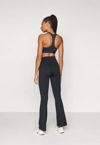 Čierna atletická športová podprsenka a nohavice s vysokým pásom, s hladkou textúrou a priliehavým strihom, doplnené bielymi teniskami.