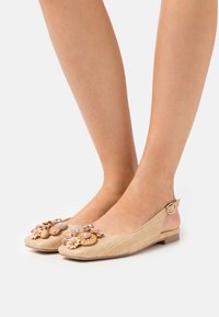 Bailarinas beige con tiras traseras y adornos florales, hechas de material texturizado. Tienen una puntera redondeada y detalle de hebilla en el tacón.