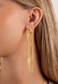 Orecchini d'oro con un design a nodo attorcigliato nella parte superiore, con più filamenti allungati che pendono verso il basso, creando un aspetto elegante e lineare.