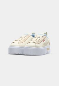 Beige Leder-Sneaker mit hellblauen Akzenten, flachen Schnürsenkeln und einer dicke weißen Sohle mit strukturierten Details. PUMA-Logo in Rot an der Seite.