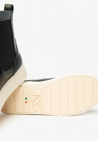 Czarne skórzane botki Chelsea z beżową gumową podeszwą, z napisem "Made in Italy" oraz włoską flagą na dolnej stronie podeszwy.