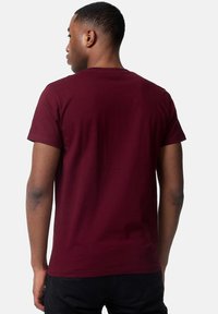 Tricou scurt de culoare cărămizie, cu guler rotund. Fabricat din bumbac moale, are o textură fină și spatele simplu, fără imprimeuri sau accente.