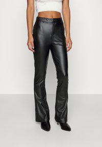 Woman wearing high-waist black faux leather pants and black pointed-toe heeled boots, cropped white top visible above waist.