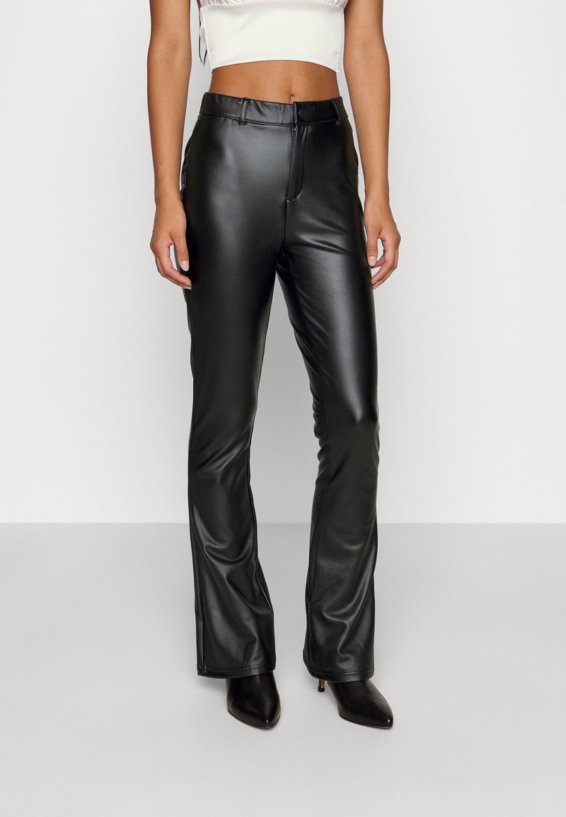 Woman wearing high-waist black faux leather pants and black pointed-toe heeled boots, cropped white top visible above waist.