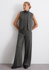 Gray pinstriped vest with a mock neck top and matching wide-leg trousers. Textured fabric, fitted waist, and black platform shoes.