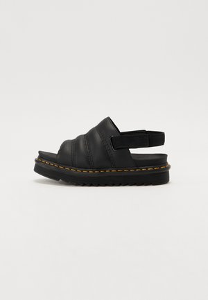 Schwarze Leder-Sandale mit offenem Zehenbereich, gepolsterten Riemen, verstellbarem Riemen hinten, dicker profillierter Sohle und gelber Naht entlang der Sohlenkante.