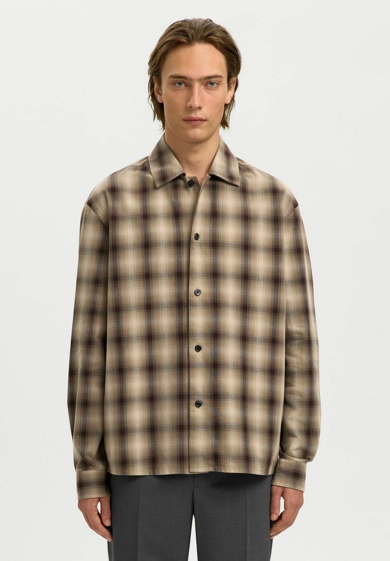Camisa de cuadros de manga larga en tonos beige, marrón y tostado. Presenta un cierre de botones en la parte delantera, textura suave y corte relajado. Diseño de cuello clásico.