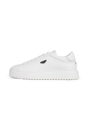 Zapatilla blanca de corte bajo con suela gruesa estriada, cordones blancos y pequeño logotipo hexagonal negro y plateado en el lateral.