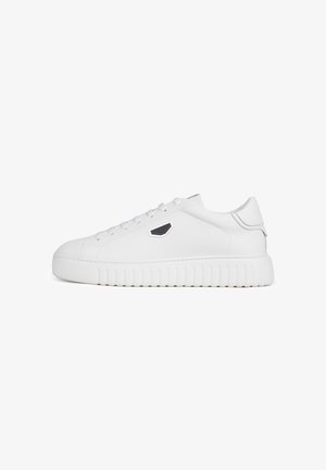 Zapatilla blanca de corte bajo con suela gruesa estriada, cordones blancos y pequeño logotipo hexagonal negro y plateado en el lateral.