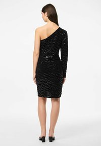 Juoda blizgučiais puošta suknelė, su viena petneša ir prigludusia forma. Tekstūruotas raštas su šiek tiek asimetrišku kirpimu. Iki kelių, prigludusi.