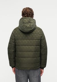 Zelena podstavljena jakna s kapuljačom, s teksturiranim uzorkom. Rukavi su elastični i ima ravni kroj. Prikladna za hladno vrijeme.