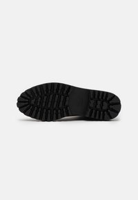 Black rubber shoe sole featuring a tread pattern with varying depths and grooves for traction, flat heel design, and a rounded toe.