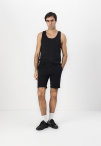 Conjunto de top sin mangas negro y pantalones cortos negros. El material parece ser de algodón. Pantalones cortos de longitud media con bolsillos laterales. Zapatillas negras y calcetines blancos.