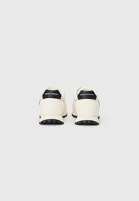 Baltas čības ar melnu papēža akcentu. Materiāli izskatās viegli un ir ar gludu tekstūru. Uz aizmugures ir redzams logs, un tām ir izturīgs zole.