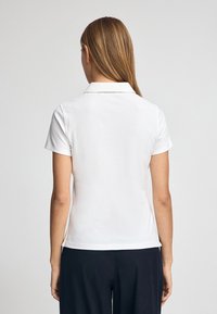 Biała koszulka polo z kołnierzykiem, krótkimi rękawami i gładką fakturą. Lekko casualowy krój, z bocznymi rozcięciami u dołu.