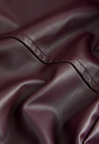 Tejido de imitación cuero burdeos con una superficie texturizada, que presenta suaves arrugas y delicados detalles de costura.