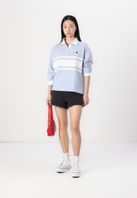 Svetlo modra polo majica s dolgimi rokavi in belimi črtami, nosi se z črnimi denim kratkimi hlačami. Obleko dopolnjuje rdeča torbica in bele športne superge.