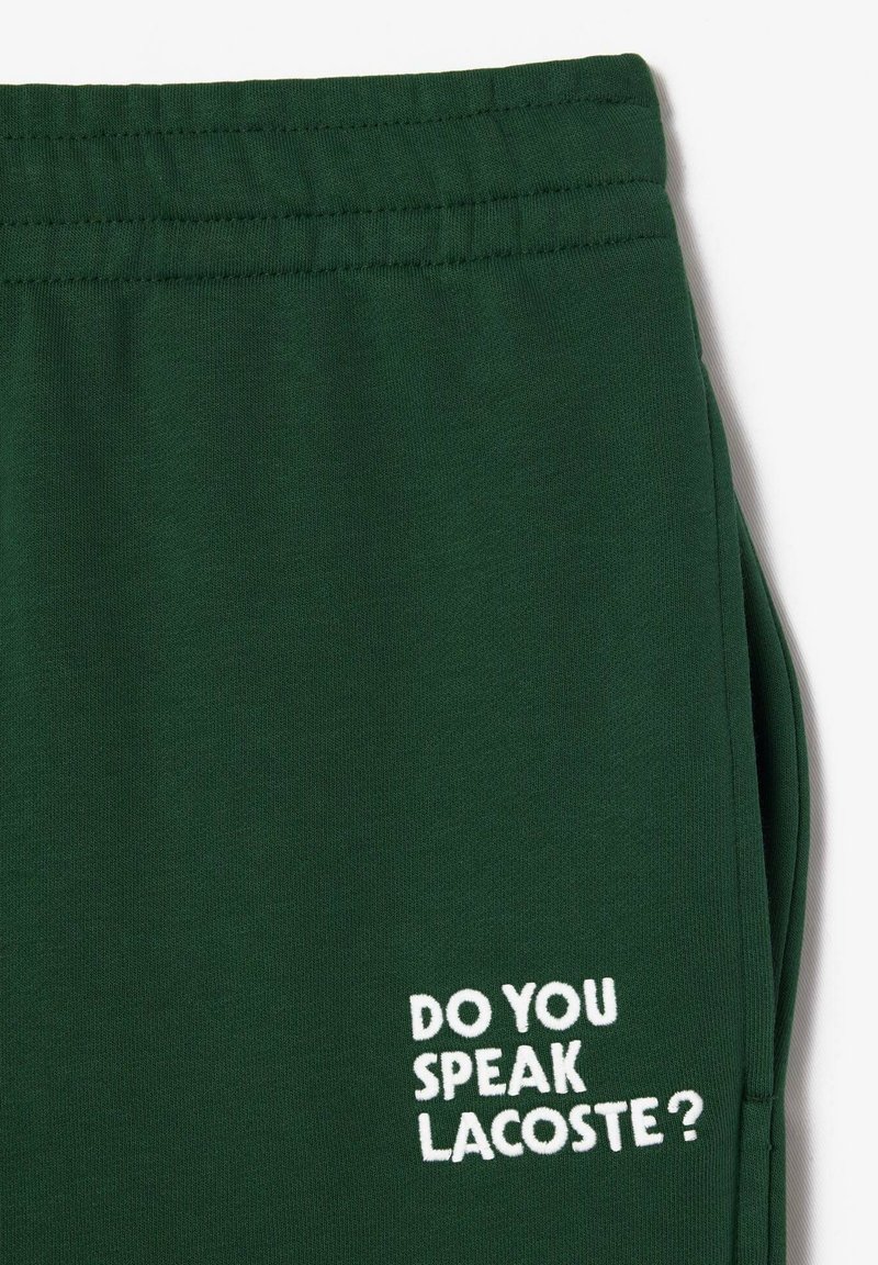 Ciemnozielone dresy z elastycznym pasem i haftowanym napisem "CZY MÓWISZ LACOSTE?" w białym kolorze, umieszczonym na nodze.