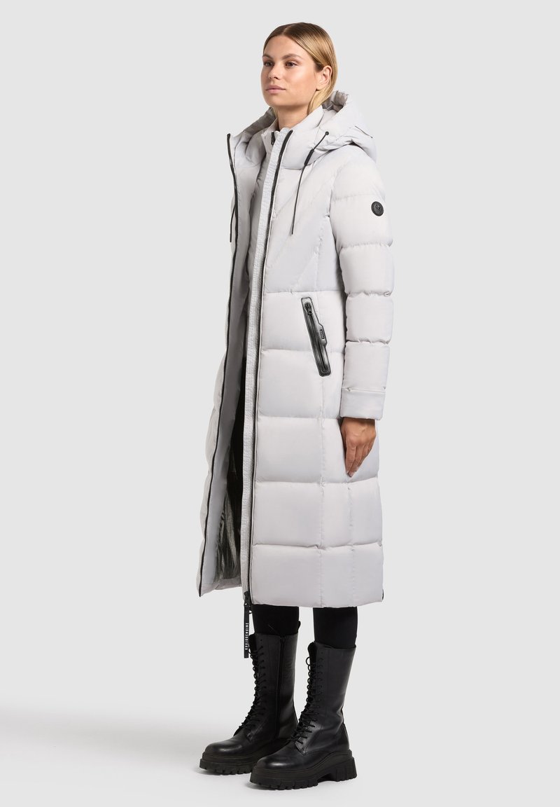Long, padded coat in light gray with a hood. Features zippered pockets and a zipper closure. Matte texture with black accents and stitching.