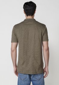 Polo de manga corta en verde oliva, confeccionado con una tela texturizada con un patrón sutil, que presenta un corte relajado y un diseño de cuello clásico.