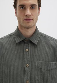 Grüne Cordhemd mit Knopfleiste, Kragen, strukturiertem Stoff und Brusttasche. Braune Knöpfe verleihen dem Design das gewisse Etwas.