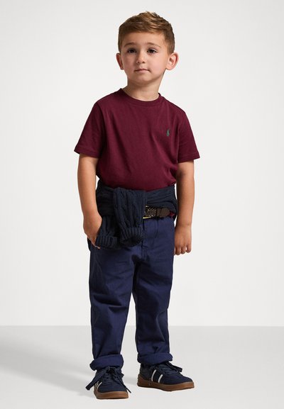 Μαρούλι μπλουζάκι κοντό μανίκι, ναυτικές παντελόνες, ναυλική ζακέτα δεμένη στη μέση, καφέ αθλητικά παπούτσια με λευκές ρίγες. Απλή, κλασική ενδυμασία για παιδιά.