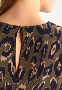 Brązowy i granatowy materiał w serek w panterkę z detalem w formie otworu na plecach, z małym okrągłym zapięciem na guziki na karku. Gładka faktura.