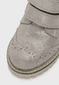 Botte en suède grise pailletée avec un bout arrondi, des perforations décoratives, deux sangles Velcro réglables et une semelle texturée.