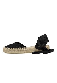 Espadrille negra con parte superior de lona, suela de yute y un borde trenzado. Presenta largas cintas negras alrededor del tobillo para un ajuste seguro.