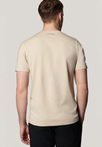 Beżowa bawełniana koszulka z krótkim rękawem i okrągłym dekoltem. Posiada subtelne logo marki na górnej części pleców. Gładka tekstura, luźny krój.