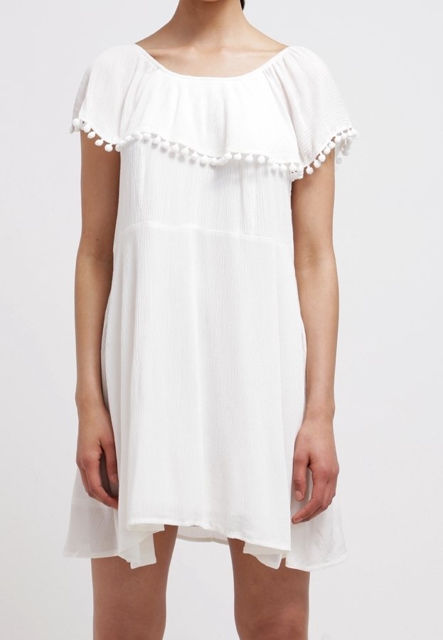 Vestido blanco texturizado con cuello redondo, volantes en capas y ribete de pompones en las mangas. Silueta en A con la parte trasera ligeramente más larga.