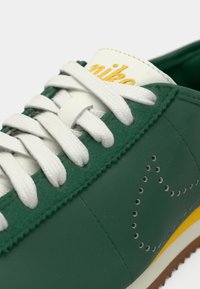 Gros plan sur une sneaker verte avec des lacets blancs, un texte de logo jaune sur la languette et un motif de perforation en forme d'étoile sur le côté.