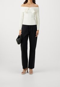 Cremefarbenes Schulter-freies Rippstrickoberteil mit umgeschlagenem Kragen, kombiniert mit hoch taillierten schwarzen Jeans mit weitem Bein und Riemchen-Heels.