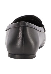 Sort læder slip-on sko set fra bagfra, der viser den glatte tekstur, sømdetaljer og lav flad sål mod en hvid baggrund.