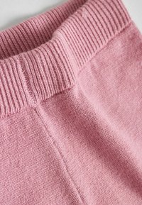 Miękki, różowy materiał z prążkowanym pasem. Tkanina ma teksturowany wygląd, z wyraźnymi detalami ściegów.