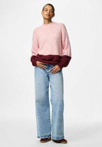 Svijetlo ružičasti pleteni džemper s tamnocrvenim rubovima i manžetama, nosi se uz svijetloplave široke traperice i smeđu obuću. Glatka tekstura.