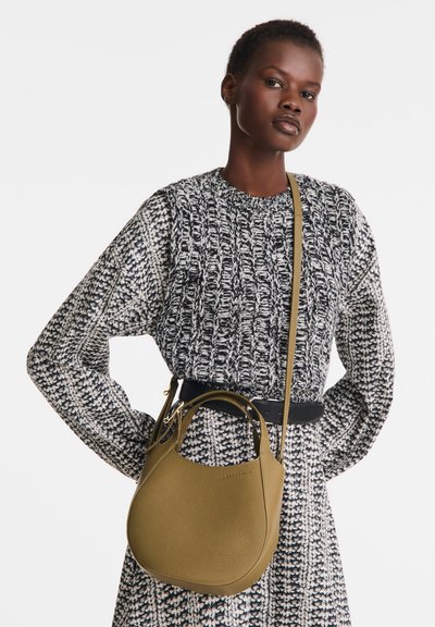 Olive green leather handbag with a rounded shape, textured surface, and dual handles. Worn with a patterned black and white sweater.