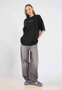 Sort oversized t-shirt med teksten "Day Dreamer" i lys lilla, parret med lysegrå brede jeans og lilla sneakers med hvide striber.
