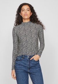 Top à manches longues en noir avec des motifs abstraits blancs. Fabriqué en tissu extensible, design ajusté, associé à un jean taille haute bleu.