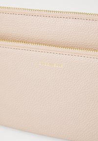 Textured pink leather pouch with a gold zipper, featuring the embossed brand name "Coccinelle" in gold on the front.