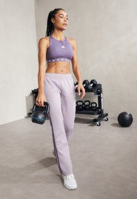 Lilla sports-bh med teksturert design, kombinert med lyse lilla treningsbukser med sidestriper. Holder en svart kettlebell.