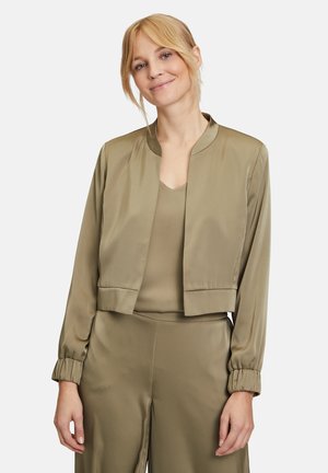 Olivgrüne, satinierte Bomberjacke mit einem taillierten Design, rundem Kragen und elastischen Bündchen, getragen über einem passenden Oberteil. Glatte Textur.