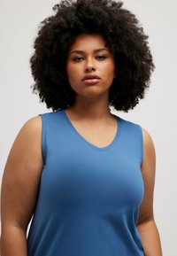 Mouwloze V-hals top in een effen blauwe kleur, met een gladde textuur en een relaxte pasvorm. De stof lijkt lichtgewicht en ademend.