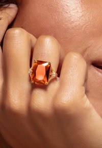 Grosse bague en pierre précieuse orange rectangulaire avec des accents en or. Le design clair présente de petites pierres latérales et une finition polie.