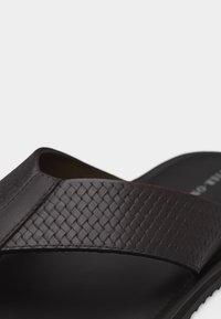 Κοντινό πλάνο σκούρου καφέ σανδαλιού με υφασμένο δερμάτινο λουρί πάνω από μαύρη σόλα.