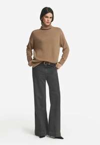 Beige Rollkragenpullover aus weichem Material, lockere Passform, mit gerippten Bündchen. Kombiniert mit hochgeschnittenen, weit geschnittenen grauen Jeans.